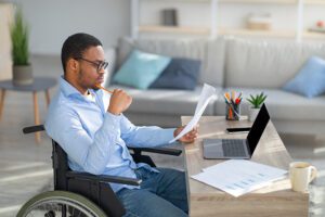 Disabled man in wheelchair sitting at a desk and reading a printout.