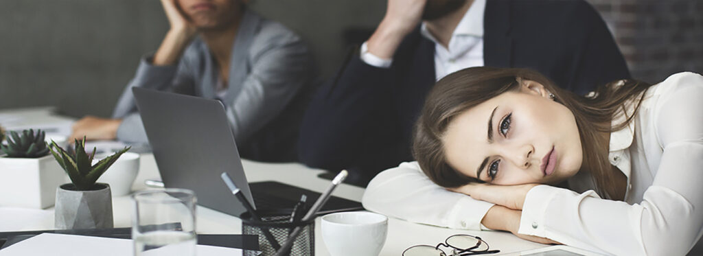 Tired woman laying her head on conference table while 2 other employees look perplexed.